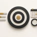 A charcoal target with a gold centre, progress bars, a calendar and a magnifying glass.