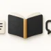 An open charcoal book beside a cream note sheet and a single speech bubble.